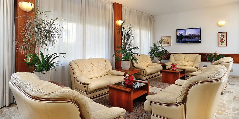 Salle de séjour élégante avec des canapés en cuir beige, des plantes et une télévision murale.